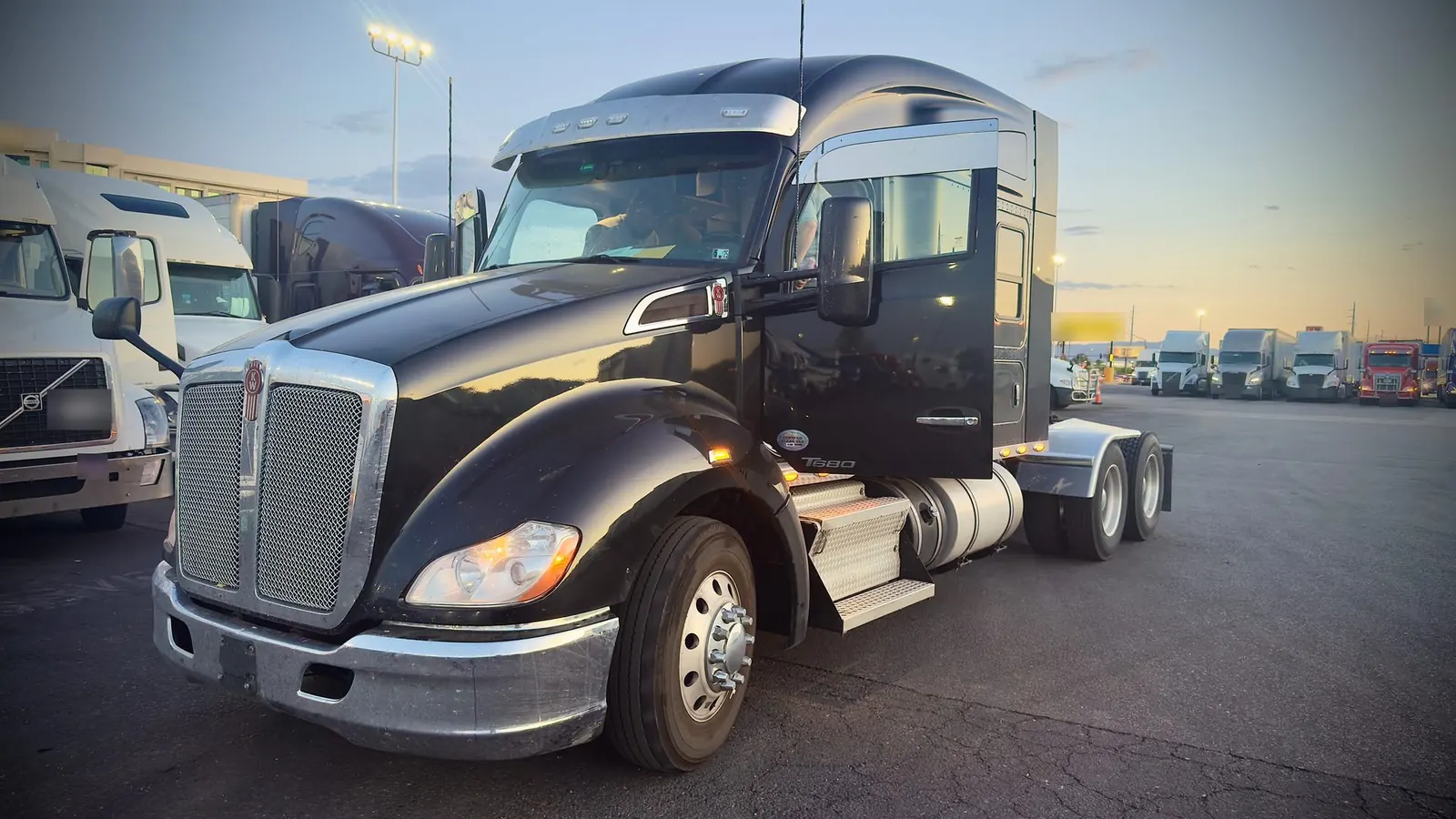 Black Kenworth T680 semi truck parked in a truck yard at dusk